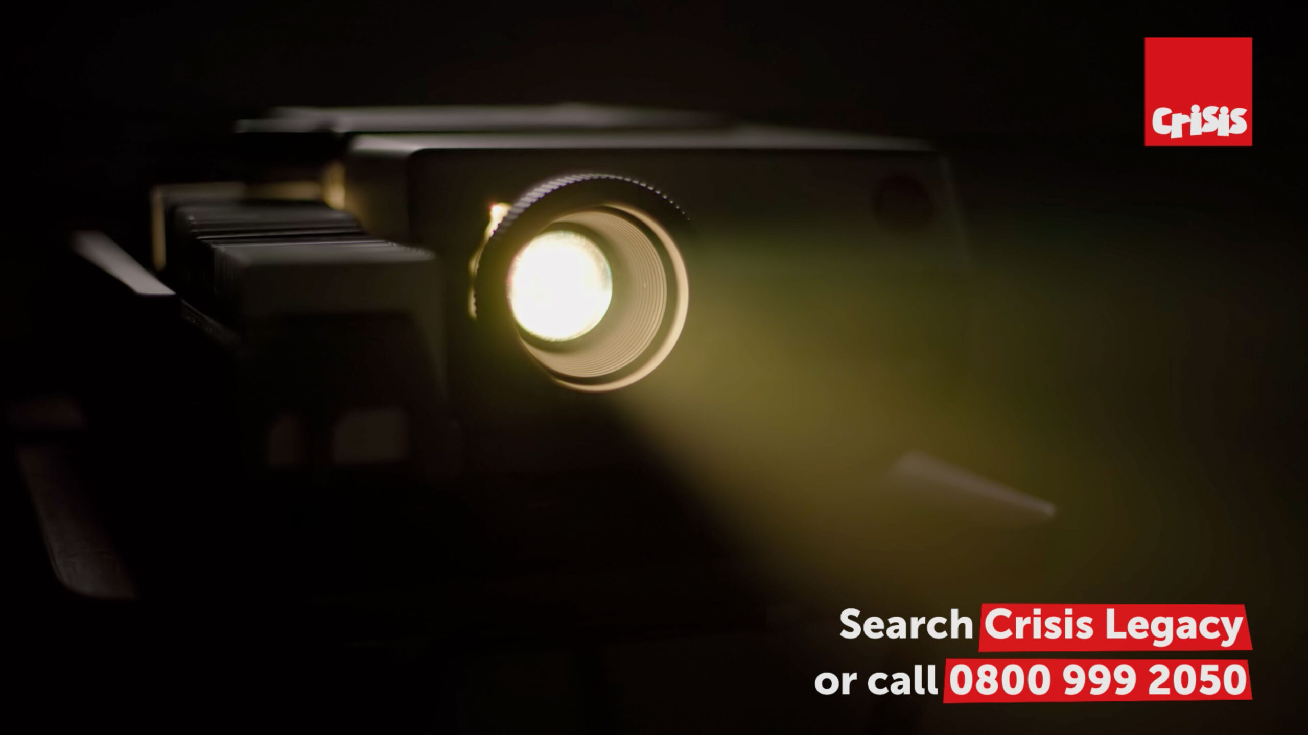 Projector in a dark room with light shining towards the viewer and details of contact information for Crisis legacy team in the bottom right.