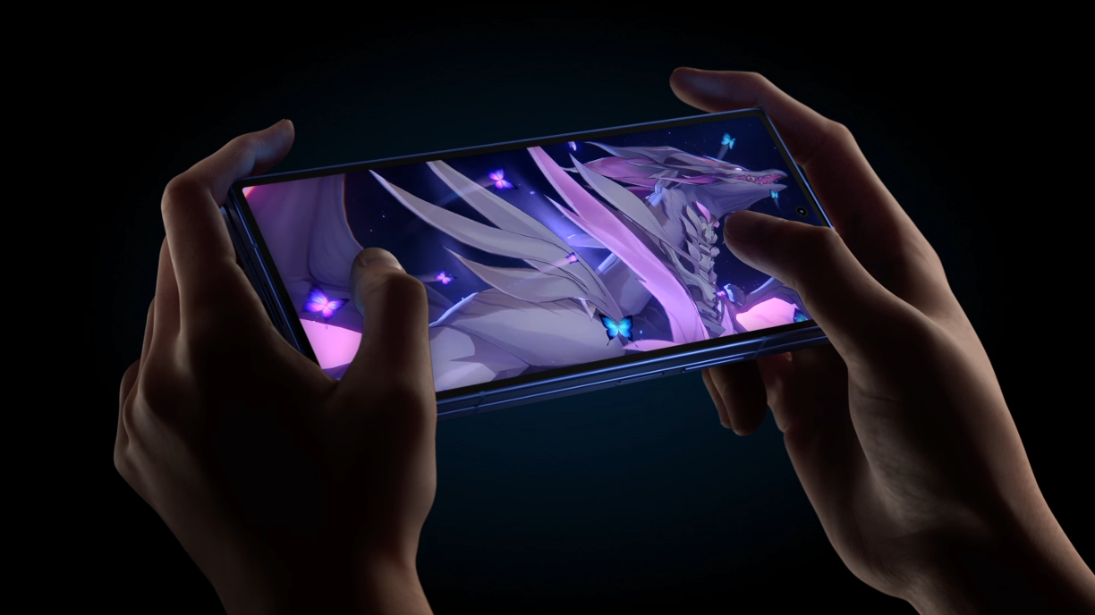 Close up of hands holding a Samsung mobile phone on a dark background, featuring a purple graphic on the phone screen.